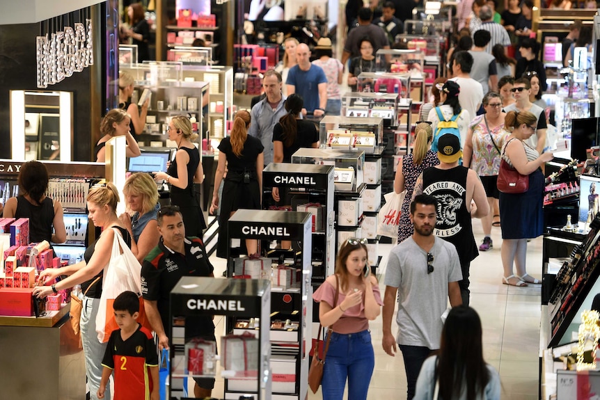 Shoppers mill around a cosmetics department in a large department store