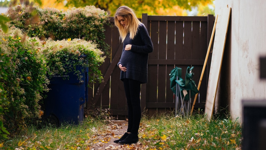 Woman holding her pregnant belly in a backyard, in a story about women embracing placenta rituals.