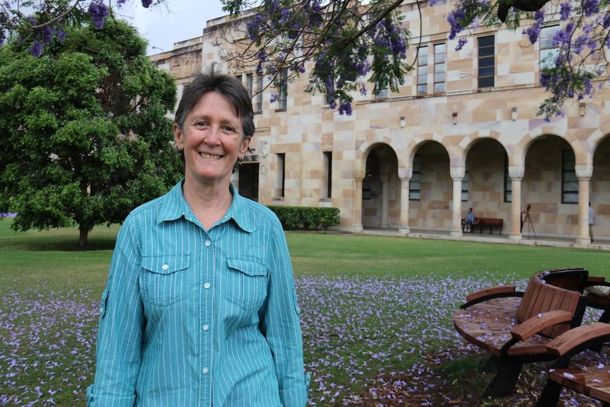 Dr Dane smiles at camera at University of Queensland's great court, with jacaranda trees framing her face.