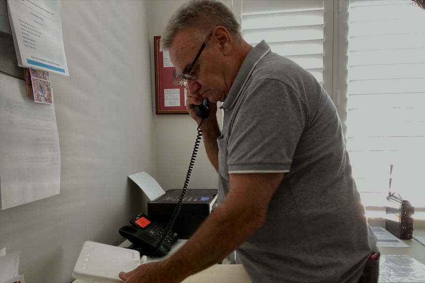 A man standing holding a phone to his ear and looking at his internet router