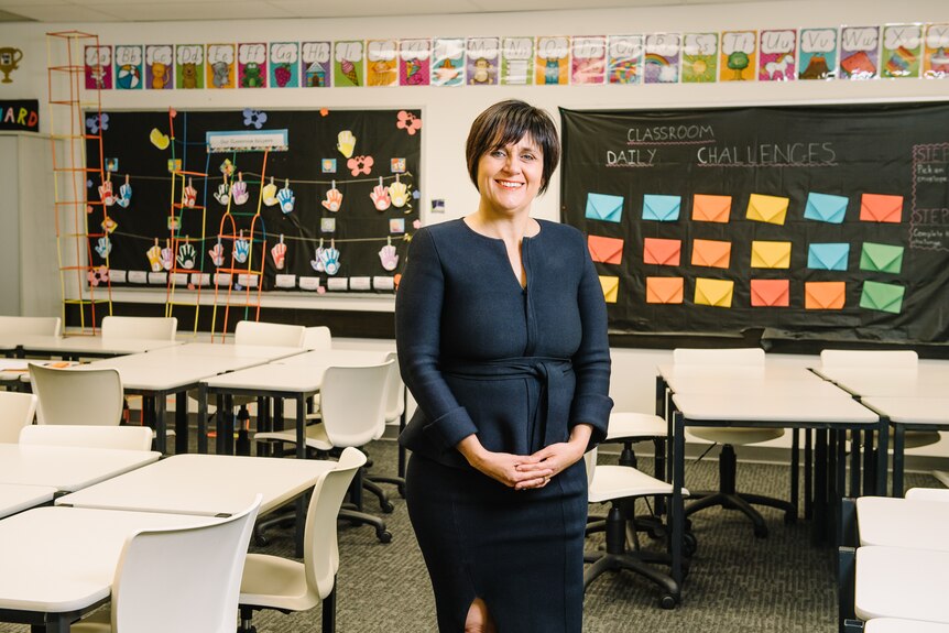 A woman wearning a black dress standing in front of a primary school classroom
