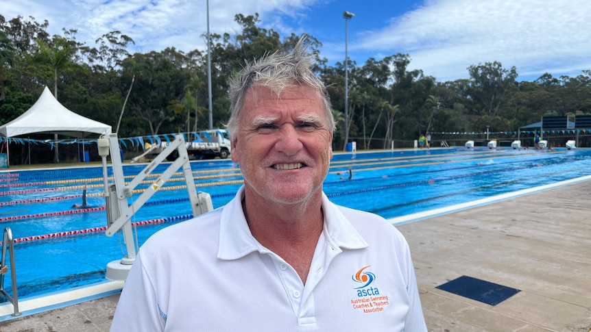 A greying haired man stands in front of a lap pool.