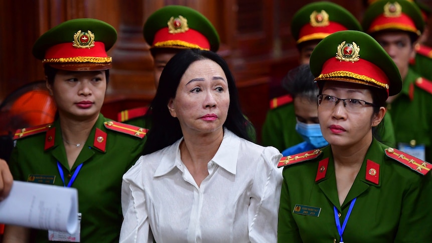 A Vietnamese woman wearing a white shirt sitting in court flanked by security women.
