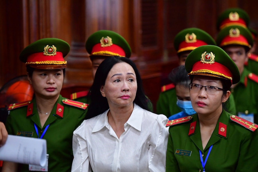 A Vietnamese woman wearing a white shirt sitting in court flanked by security women.