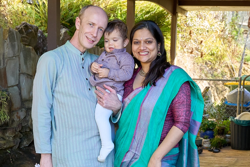 A mother and father hold their young son between them as they pose for a photograph. 