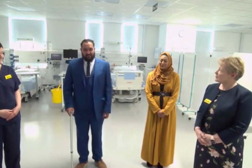 Three women and a man stand in a hospital setting with beds visible in the background.