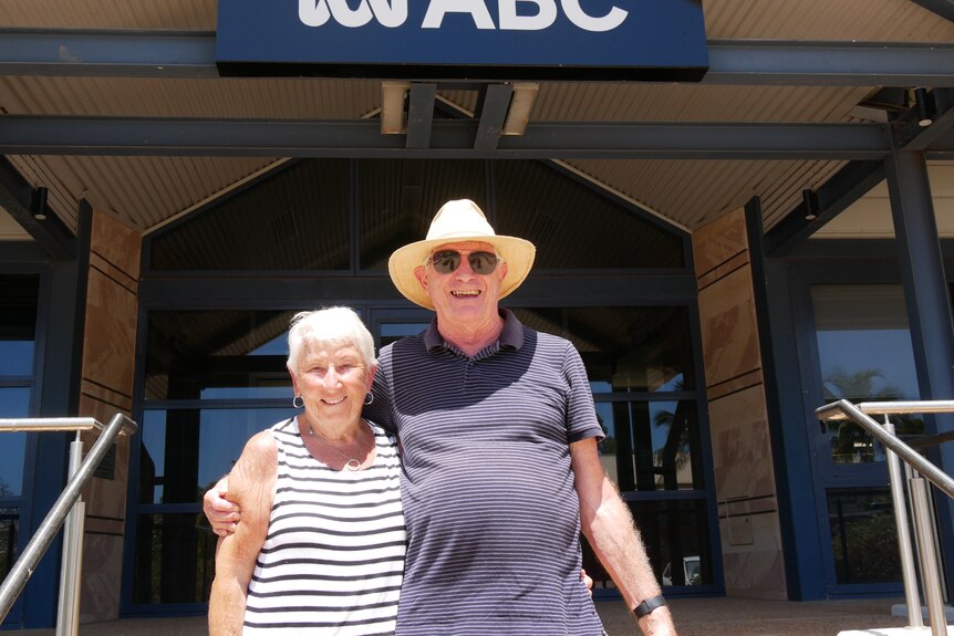 An elderly couple hugging in from of an ABC office. 