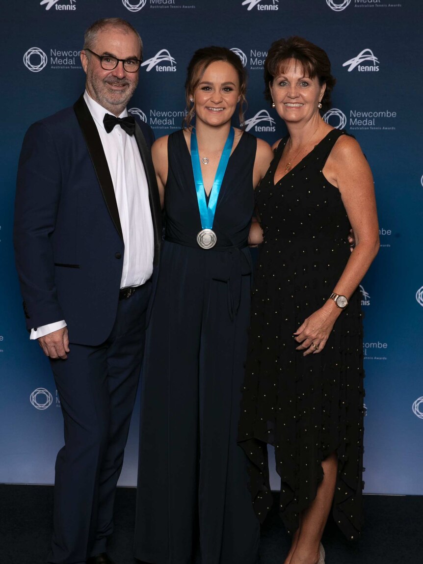 Ash Barty wearing medal flanked by her parents.