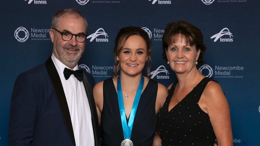 Ash Barty wearing medal flanked by her parents.