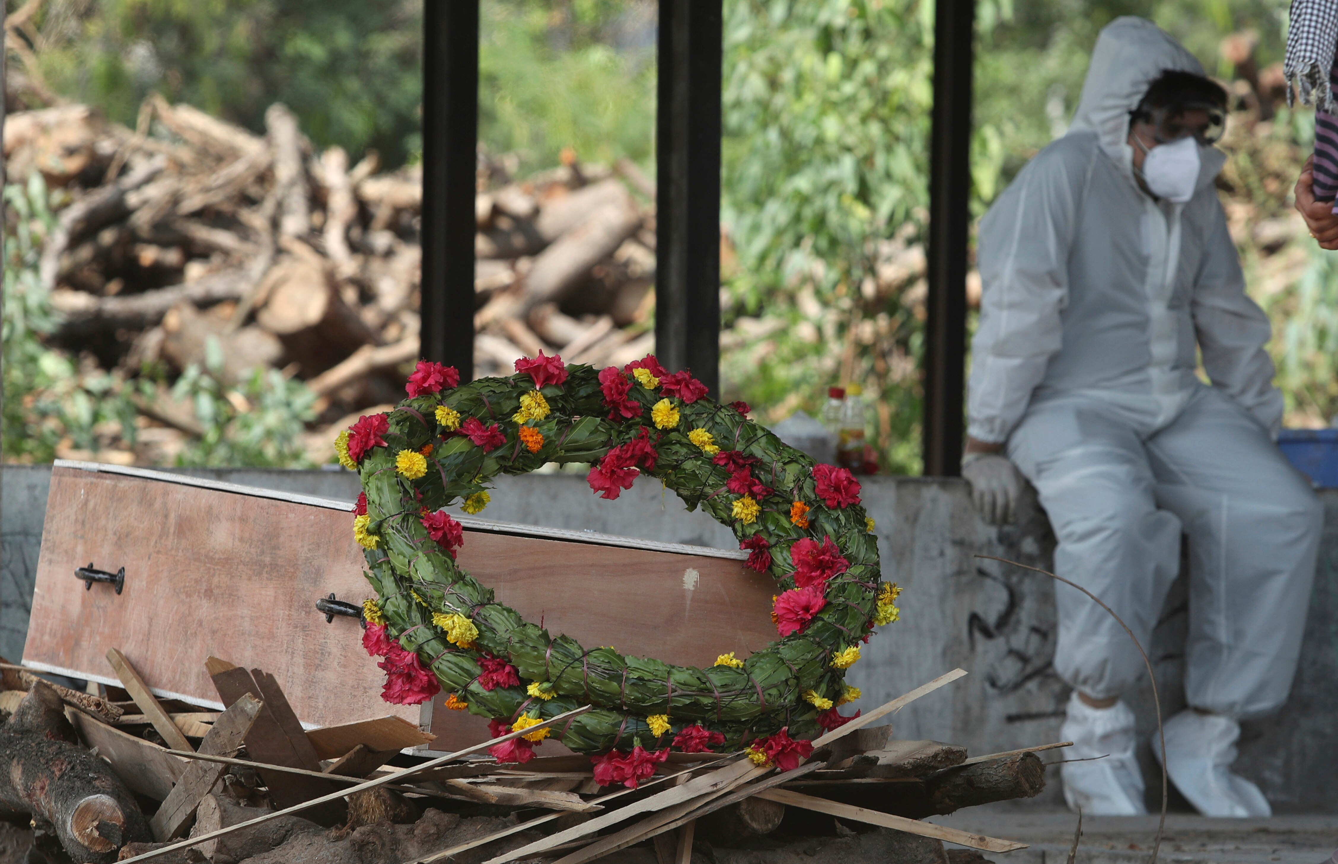 A wreath lies on the coffin of a COVID-19 victim next to a person wearing a PPE