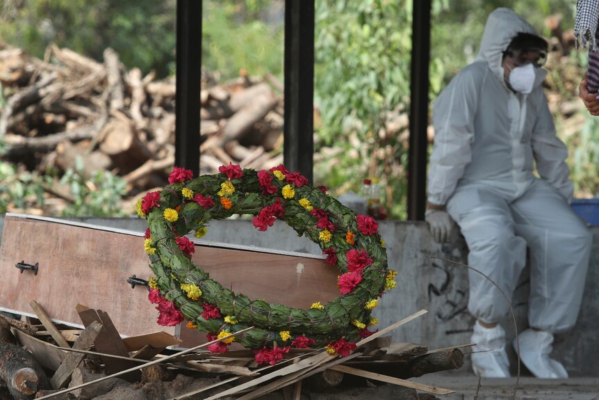 A wreath lies on the coffin of a COVID-19 victim next to a person wearing a PPE