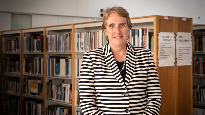 Woman stands in front of rows of library bookshelves