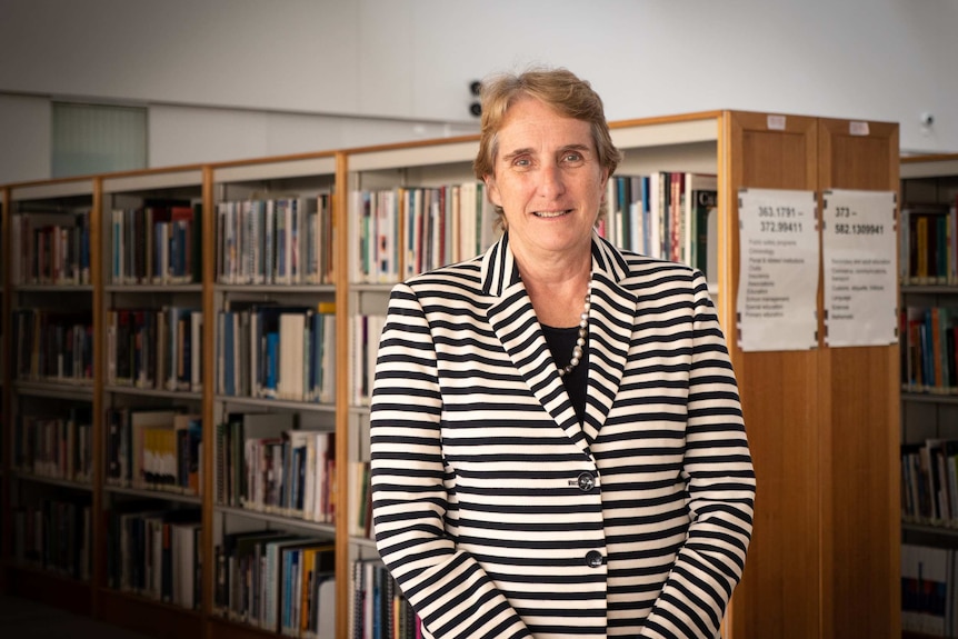 Woman stands in front of rows of library bookshelves