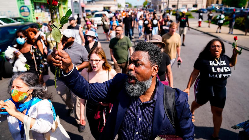 People march with fists raised to the scene of a shooting outside a supermarket.