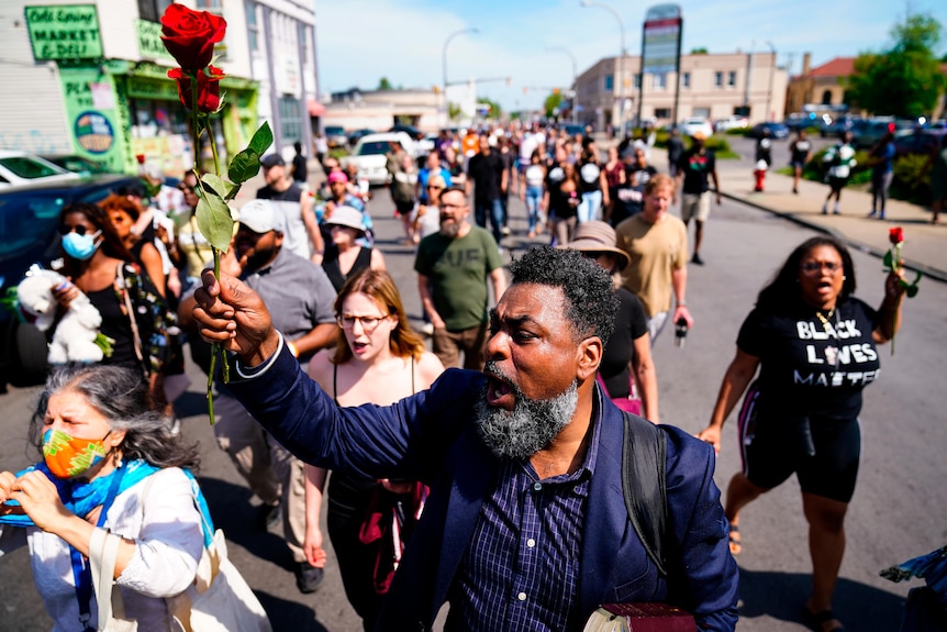 People march with fists raised to the scene of a shooting outside a supermarket.