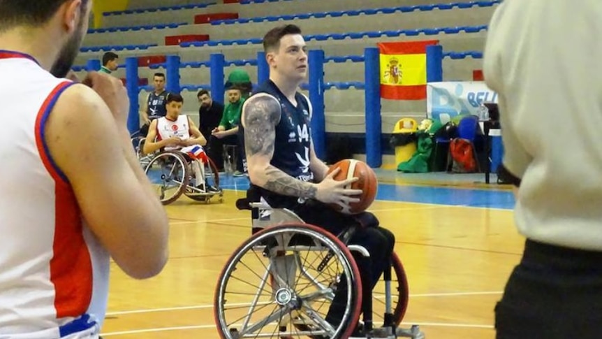 A player in a wheelchair prepares to shoot the ball, watched by a number of other people in wheelchairs.
