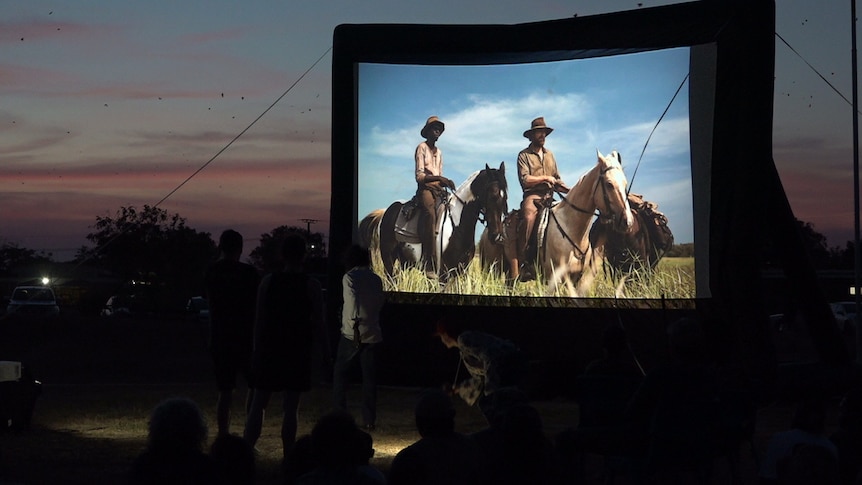 A blow up projector shows the film High Ground with footage of two men on horses in a field.