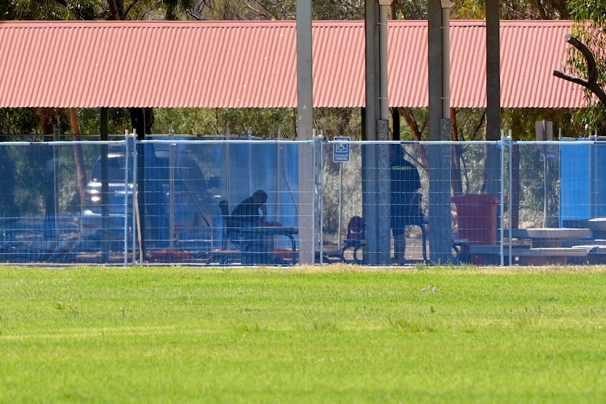 Two men wearing black shirts behind a blue fence at Willyama High School in Broken Hill. 