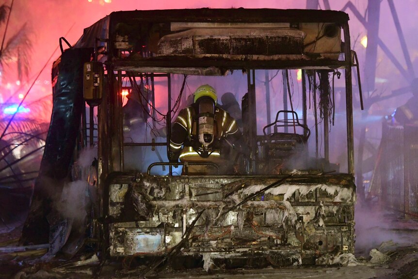 Firefighters standing in a burned out bus