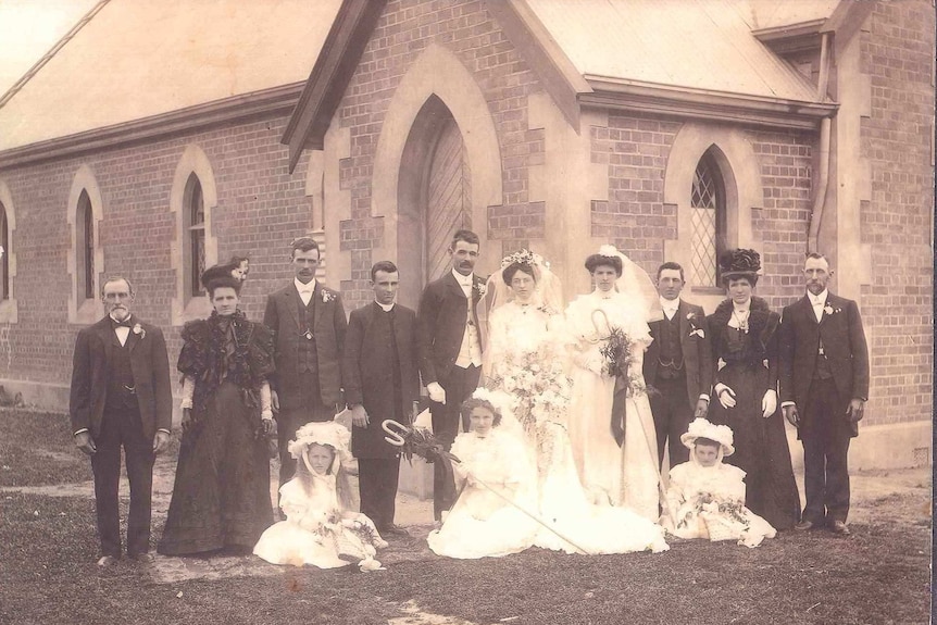 Black and white photo of a wedding party standing in front of a church.