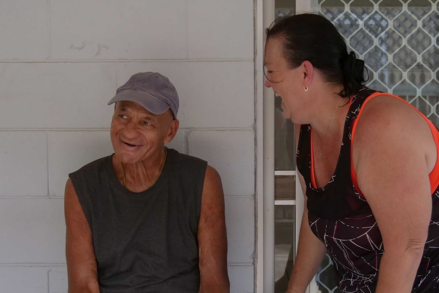 A woman stands laughing while a man sitting next to her smiles.