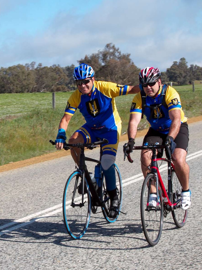 Two male cyclists ride along a country road.