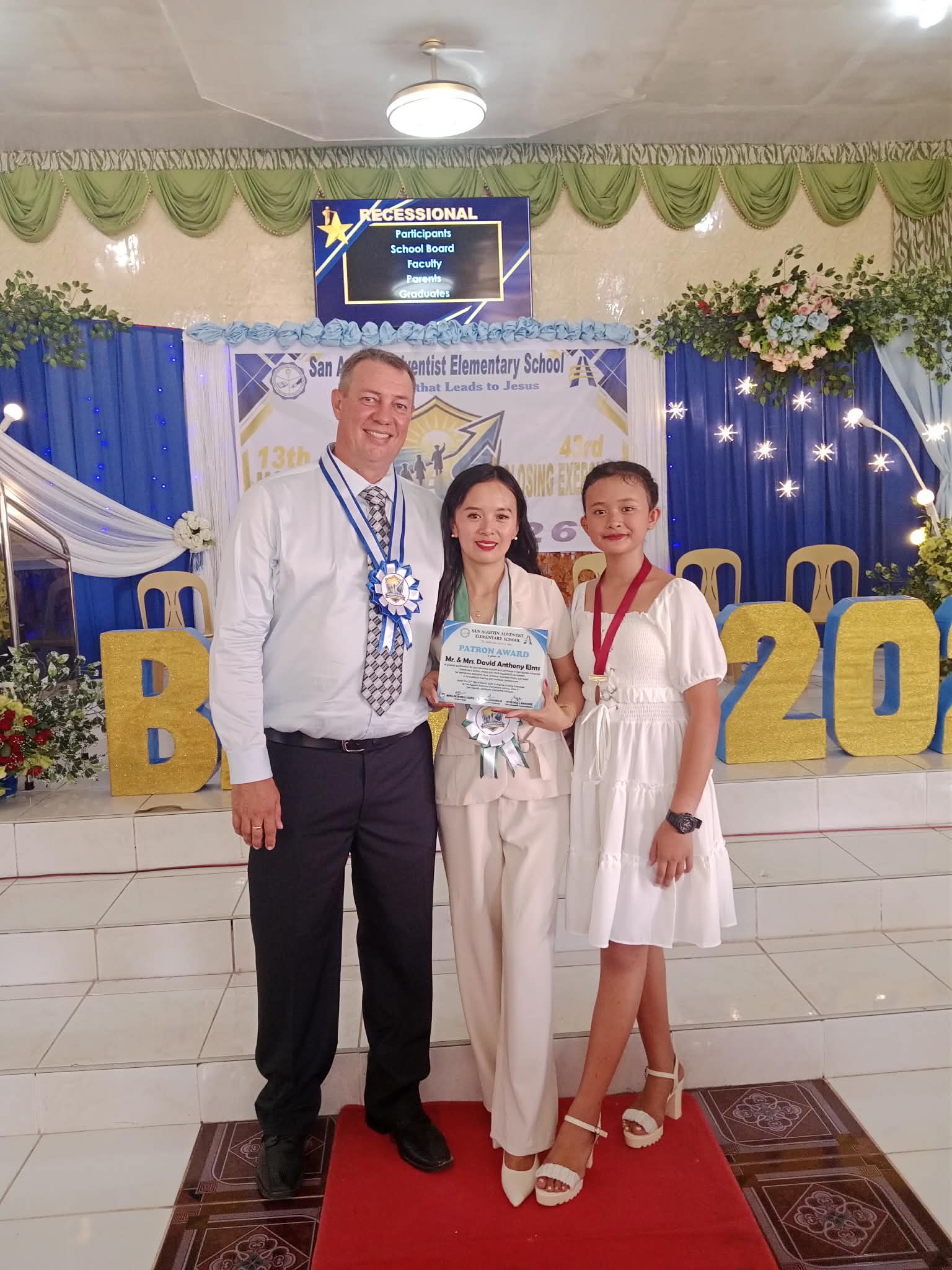 Three people standing together with the person in the middle holding a certificate