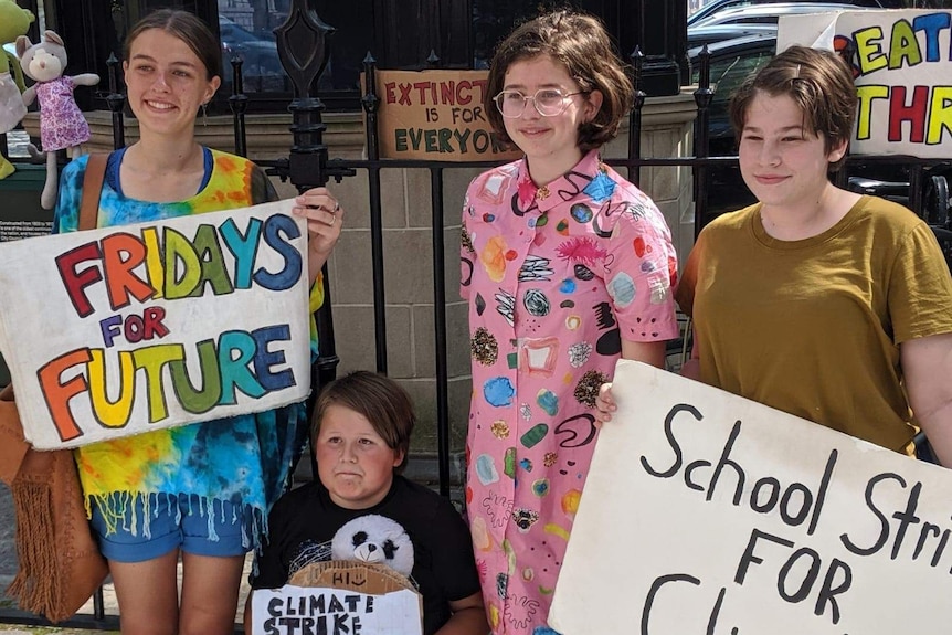Four young people stand together outside holding signs about climate change.
