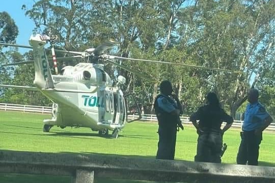 White helicoper parked on grass field, three police officers talking 