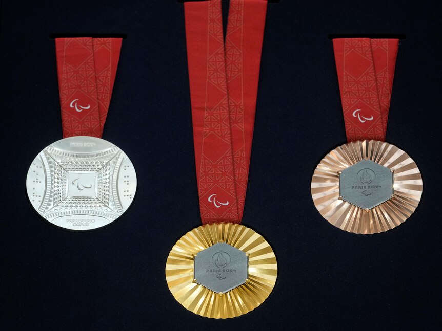 A group of Paralympic medals - silver, gold and bronze left to right - are shown against a dark background.