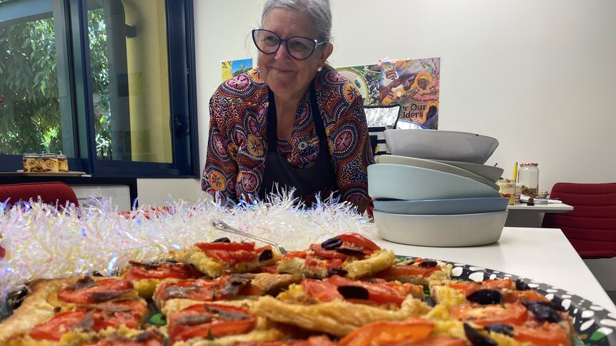 A woman in an apron stands behind a savoury tart with Christmas on top