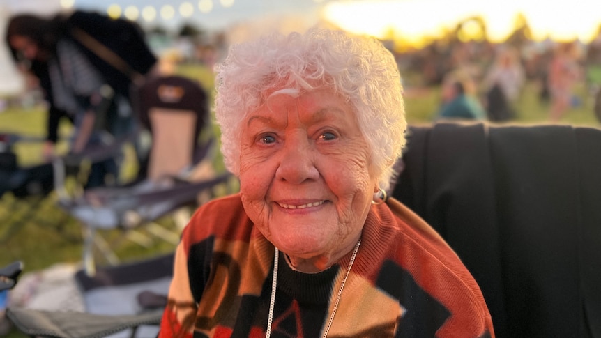 Aunty Faye Carter smiles as she sits in a camp chair on the oval.