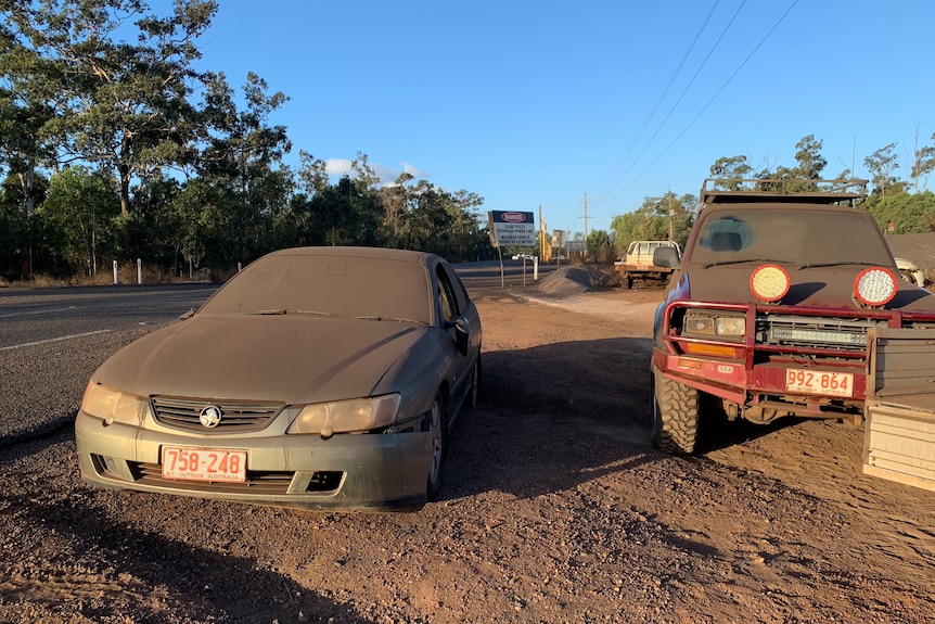 Two abandoned cars are covered in thick dust on the windshield and hood.