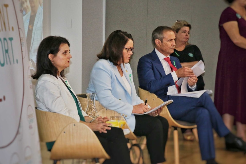 Three politicians sit at a community meeting