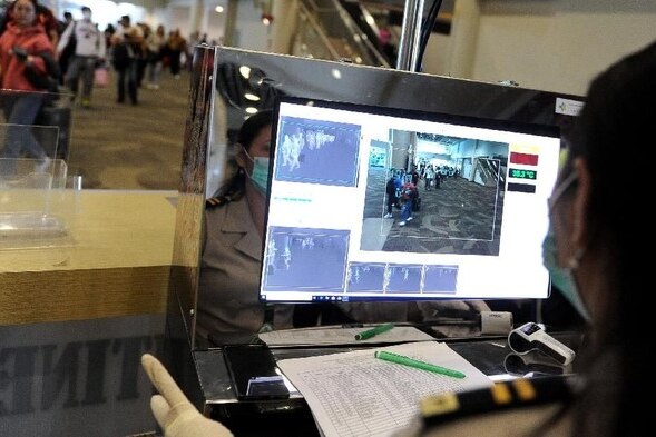 An immigration official wearing a face mask and looking at a computer screen.