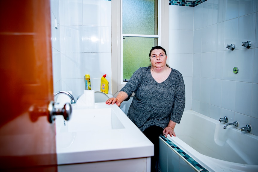 Shelly sits in the very narrow gap between her bath tub and her sink.