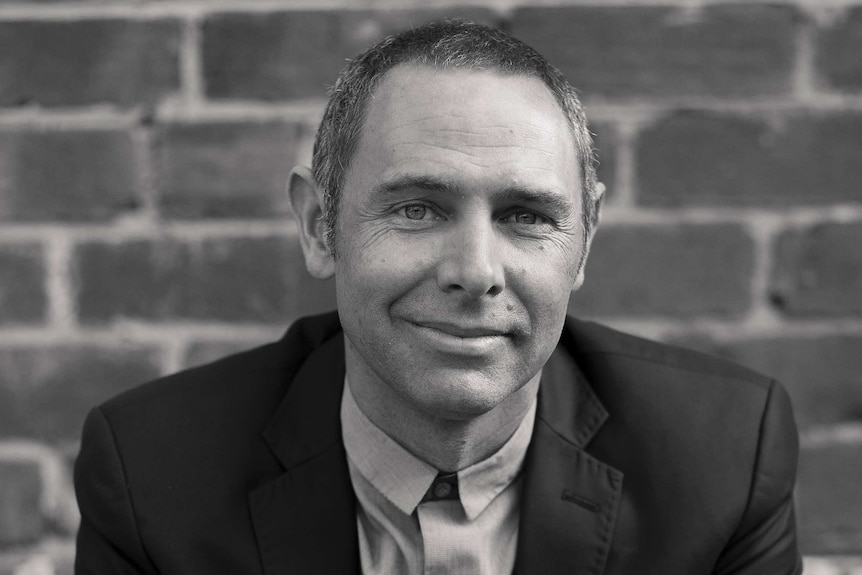 A black and white portrait of a smiling man wearing a suit.