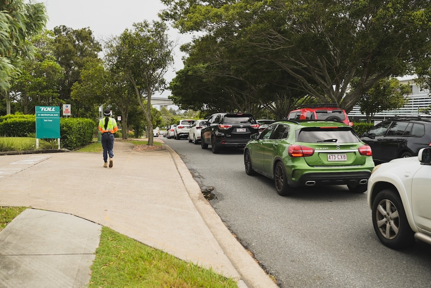 A person in a high vis shirt walks alongside a long line of cars.