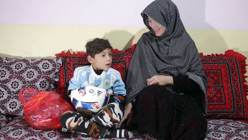 a woman sitting on a couch looks down at her son wearing an argentine soccer jersey