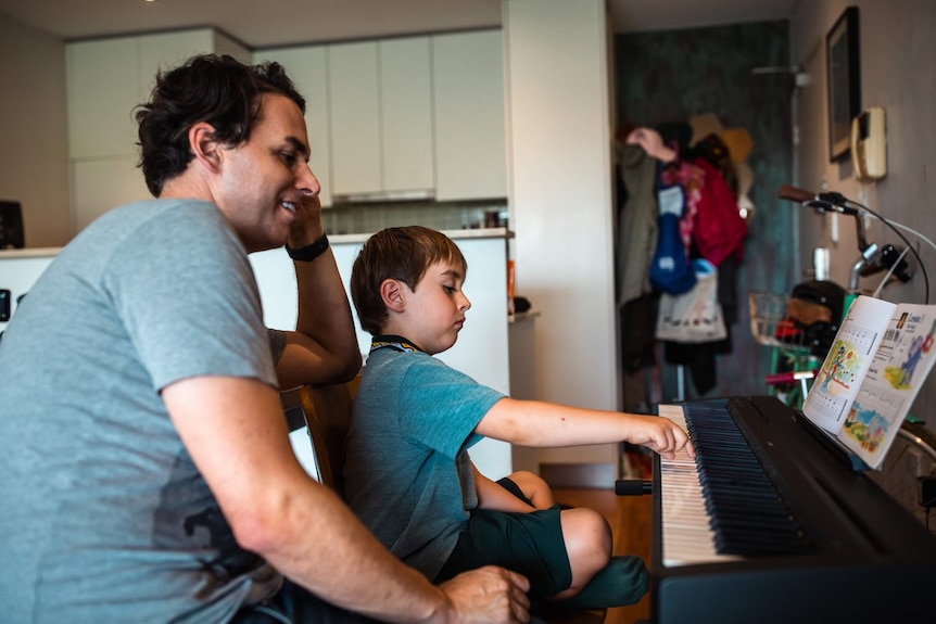 un hombre sentado junto a un niño pequeño que toca el piano