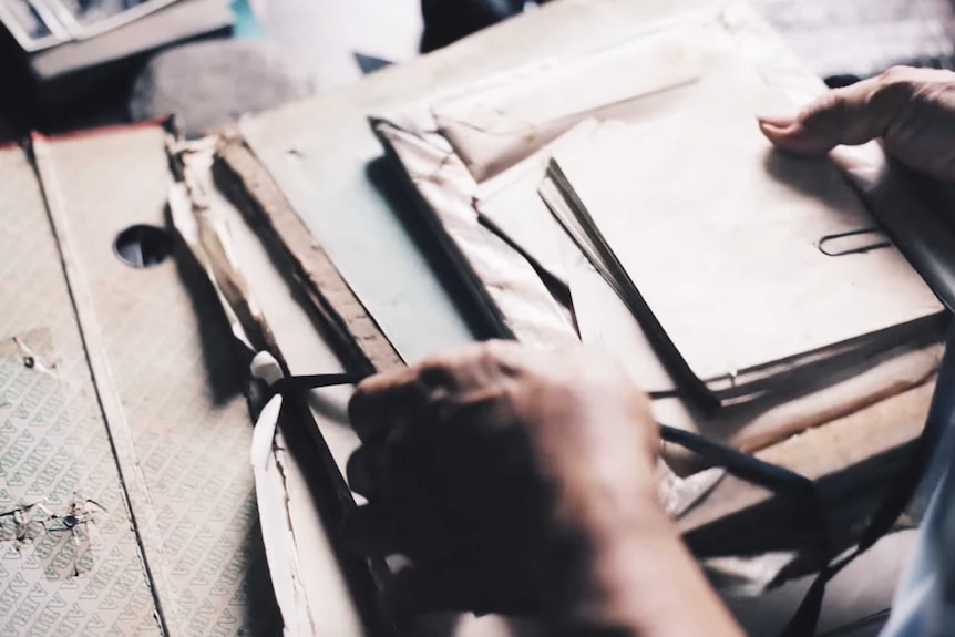 A person holding a tattered folder with envelopes and papers depicting the practice of pre-death decluttering.