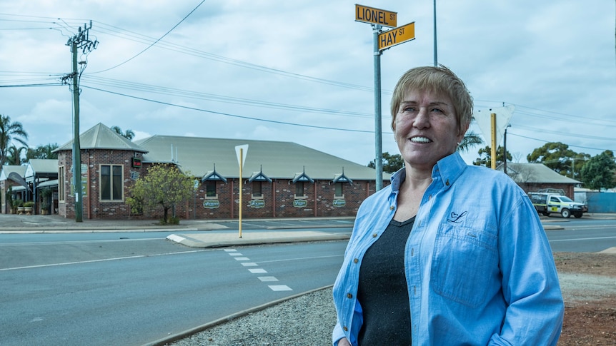 A businesswoman standing on a street corner with her property in the background.