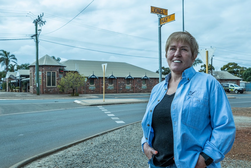 A businesswoman standing on a street corner with her property in the background.