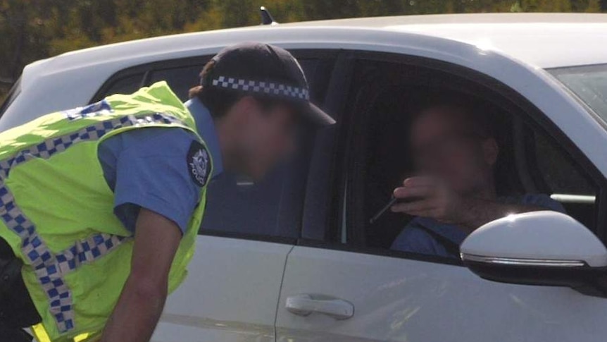 A police officer checks a man's phone to prove he is travelling for essential reasons.