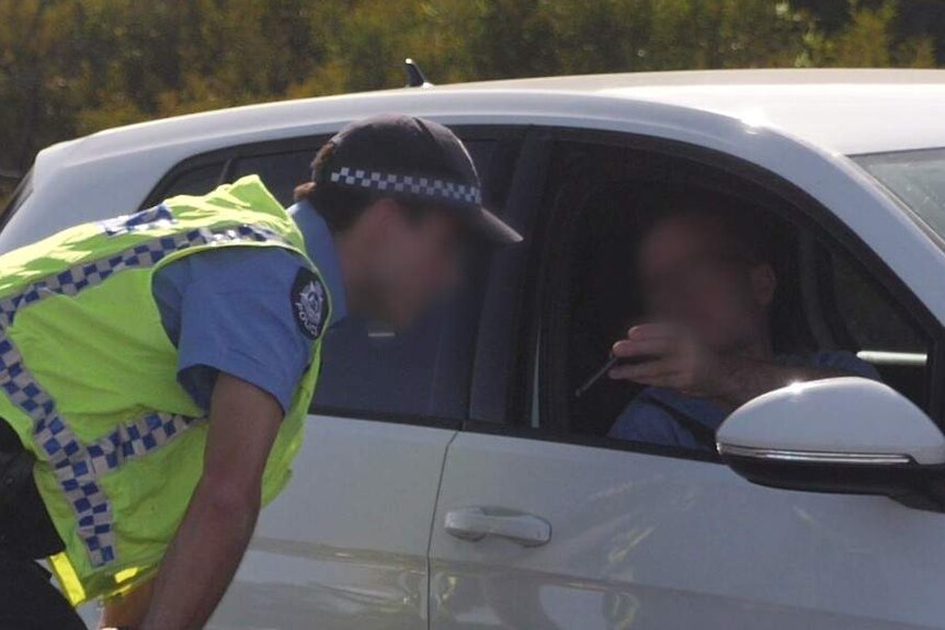 A police officer checks a man's phone to prove he is travelling for essential reasons.