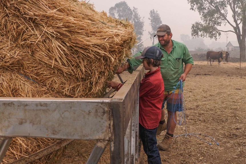 10-year-old Will and his dad Trevor lean over a cage where a bale of hay has been dropped in, they are untying the twine.