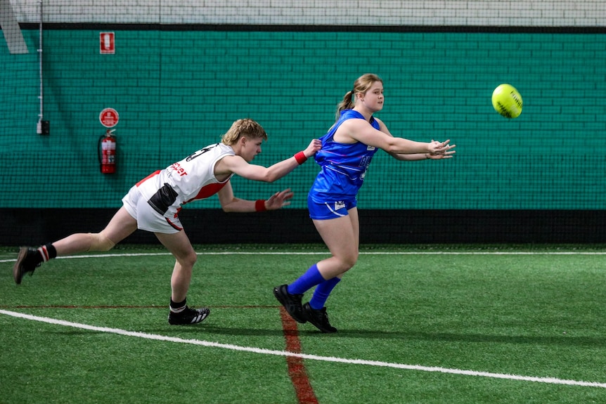 A man tackles a woman who has just handballed a football.