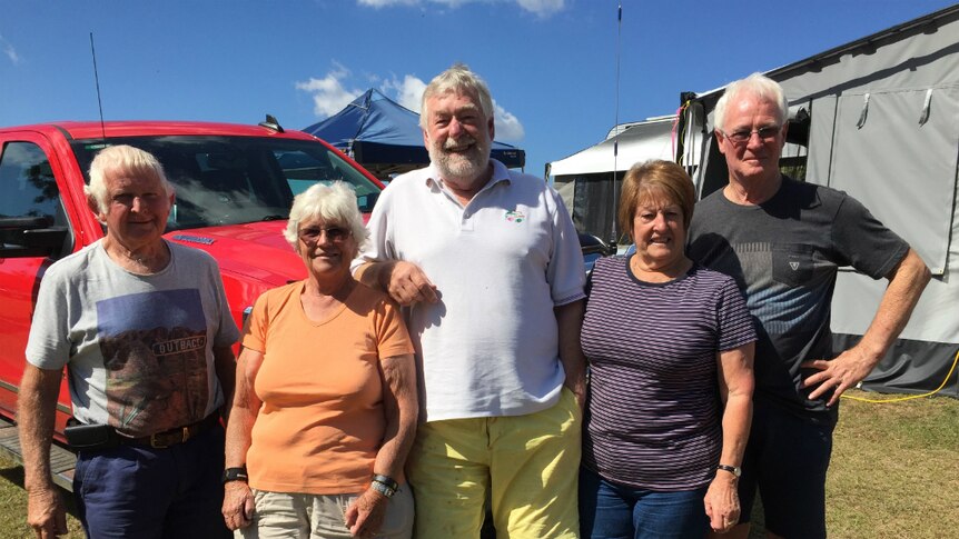 Three men and two women stand smiling at a campsite.
