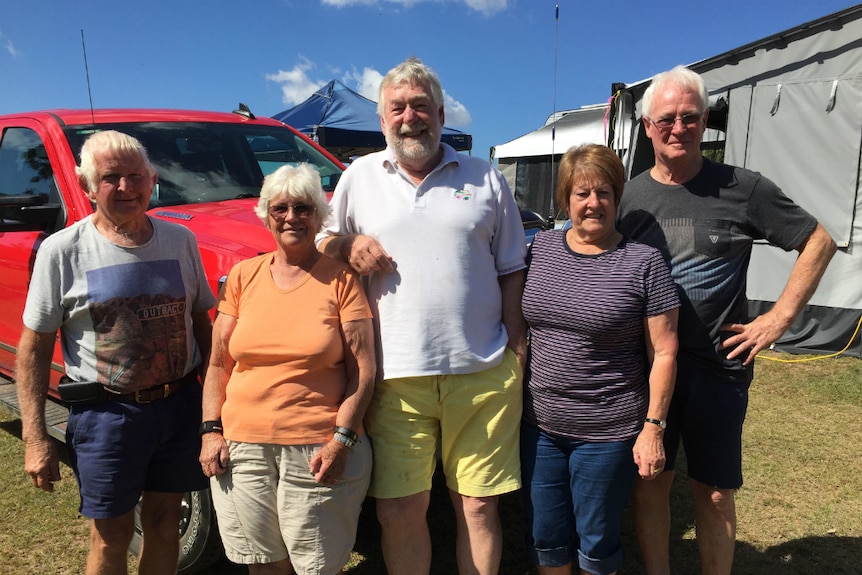 Three men and two women stand smiling at a campsite.