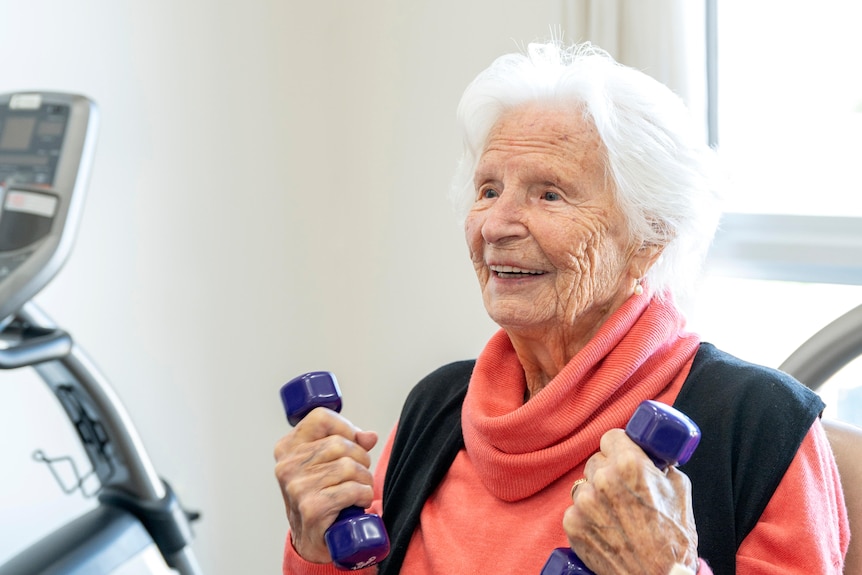 An elderly woman smiling and holding weights in her hands.
